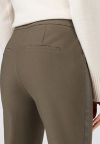 Pantalon ajusté vert olive avec une texture lisse, doté de deux poches arrière et d'une subtile bande latérale.