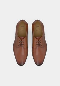 Brown leather shoes with a smooth finish, rounded toe, five eyelets, and subtle seams. "BOSS" branding visible inside. Made in Italy.