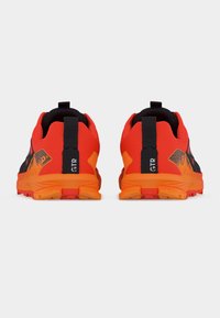 Ζευγάρι λαμπερά πορτοκαλί και μαύρα αθλητικά παπούτσια, που φαίνονται από πίσω, με μαύρες θηλιές στο τακούνι, όπου αναγράφεται η ετικέτα "GTR" σε λευκό φόντο.