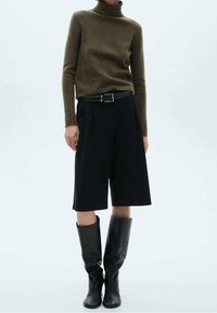 Pull à col roulé vert olive, culottes noires taille haute, bottes noires en cuir montant jusqu'aux genoux, silhouette ajustée, texture lisse, détails subtils.