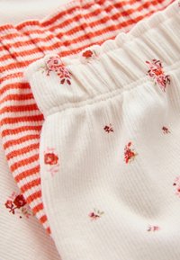 Bukser sæt med et hvidt ribbet par med blomstermotiv og et rødstreget par. Elastiske taljer og bløde stofstrukturer.