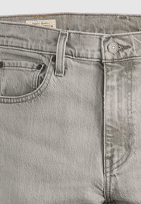 Jeans de mezclilla gris con un acabado texturizado, que presentan un diseño clásico de cinco bolsillos, herrajes metálicos y una etiqueta cosida en la cinturilla.
