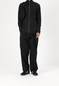 Black ribbed zip-up sweater, loose black pants, and black sneakers with white stripes; casual design with a textured finish.