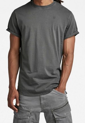 T-shirt en coton gris avec manches retroussées, encolure ronde, et petit logo sur la poitrine, associé à un pantalon cargo gris avec poches zippées.