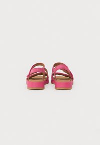 Åpne sandaler med en lys rosa semsket overdel, kryssende stropper og en flat brungul såle. Enkelt design, ingen ekstra mønstre eller beslag.