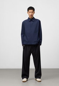 Granatowa, lekka kurtka zapinana na zamek z kołnierzykiem, dwoma przednimi kieszeniami, w połączeniu z luźnymi czarnymi spodniami i jasnymi trampkami.