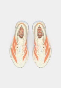 Pár běžeckých bot Adidas Adizero v krémové a oranžové barvě se bílými tkaničkami, zobrazený shora na bílém pozadí.