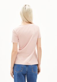 Lichtroze t-shirt met korte mouwen, een ronde halslijn en een soepele textuur, gecombineerd met blauwe high-waisted jeans met achterzakken.