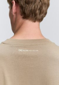 Khaki tričko s okrúhlym výstrihom, mäkkou bavlnenou tkaninou a potlačeným logom "DENIM TOM TAILOR" na zadnej časti výstrihu. Hladká textúra.