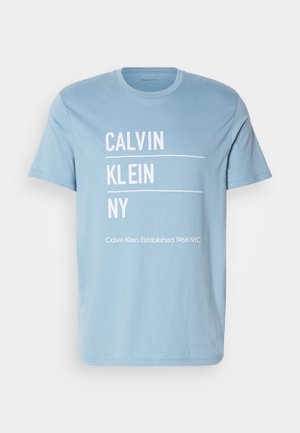 Lyseblå bomullstru-t-skjorte med hvit tekst: "CALVIN KLEIN NY" og "Calvin Klein Etablert 1968 NYC." Standard rund hals og korte ermer.