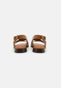 Sandales en cuir marron avec des brides ajustables, design ouvert, talon en bois et semelle intérieure texturée arborant un motif de logo circulaire.
