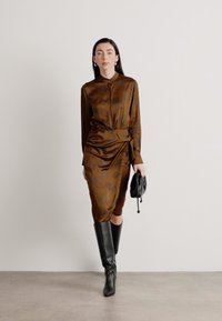 Abito in satin marrone con maniche lunghe, colletto bottonato e vita stretto. Indossato con stivali in pelle al ginocchio e una piccola borsa nera.