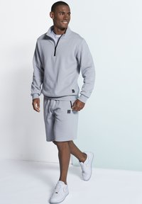 Light grey quarter-zip sweatshirt and matching shorts, made of soft fabric. White sneakers with black accents complete the outfit.