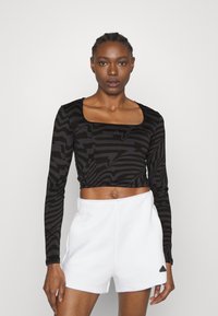 Langermet svart crop top med teksturert sebra-mønster, paret med hvite shorts; har firkantet halsudskæring og tettsittende design.