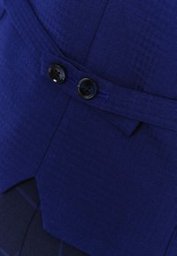 Granatowy materiał o subtelnej fakturze, z dwu guzikowym zapięciem i akcentem w postaci pasa, tworzący zorganizowany wygląd.