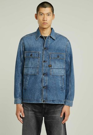 Blå denimjakke med to brystlommer, knaplukning og kontraststing. Har krave og afslappet pasform.