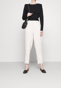 Schwarzes Langarmoberteil, cremefarbene weite Hose und schwarze Mules mit Blockabsatz. Kleine schwarze Handtasche mit einem gemusterten Riemen. Glatte Stofftextur.