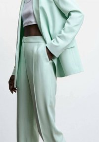 Mintgroene op maat gemaakte blazer en bijpassende broek, met een gladde stof, gestructureerd ontwerp, zijzakken en een ontspannen pasvorm.