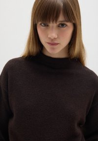Dunkelbrauner, hochgeschlossenes Sweatshirt aus weichem, strukturiertem Material. Verfügt über eine lockere Passform. Minimalistisches Design ohne sichtbare Muster oder Akzente.