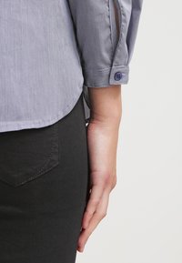 Blå och vit rutigt blus med rundad nederkant, knäppta ärmar och plisserad detalj bak, som är matchad med svarta tajta byxor.