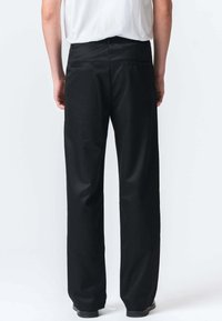 Sorte bukser med lige snit, glat stof, baglommer og en talje. Modellen har en ensfarvet hvid skjorte på ovenfor.