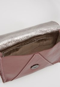 Bolso de cuero rosa con un interior metálico plateado, que presenta un cierre de presión y costuras en contraste. Acabado texturizado en el interior.