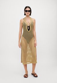 Atklāta, zelta krāsas pārklājums ar dziļu V veida kaklu, sānu šķēlumiem, virs melnā peldkostīma. Saulesbrilles un brūni sandales noslēdz izskatu.