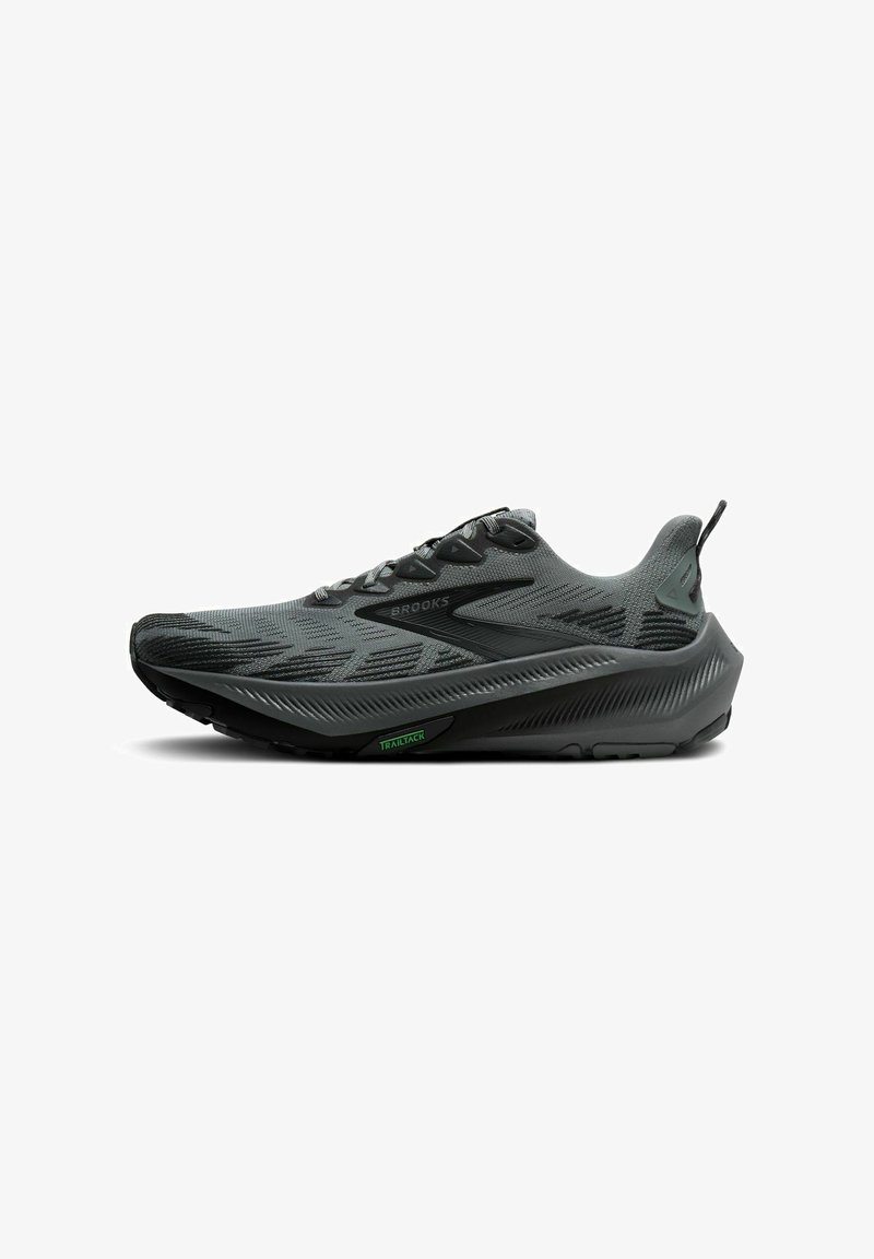Brooks running shoe in dark gray with a textured upper, reflective accents, and a cushioned sole featuring a green "TRAILTACK" detail.