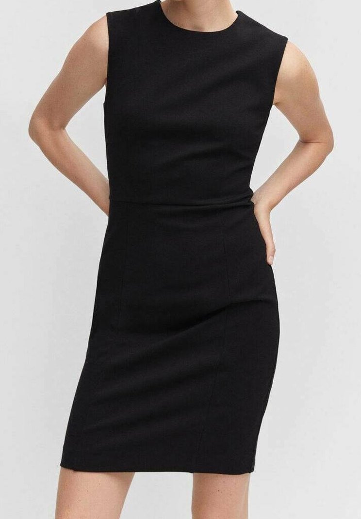 Robe noire sans manches longueur genou avec une taille ajustée portée par une personne les mains posées sur les hanches.