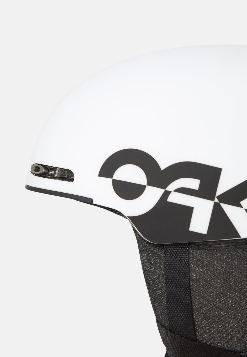 Weißer Helm mit einem großen schwarzen Logo, glatter Oberfläche und strukturiertem Riemen. Beinhaltet Lüftungsöffnungen für Luftzirkulation und hat ein elegantes, abgerundetes Design.