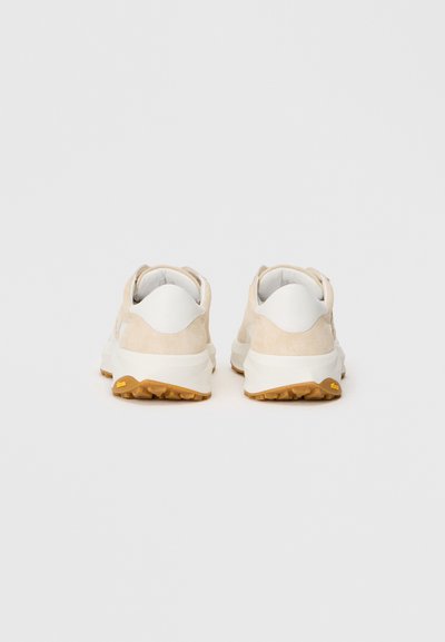 Pantofi sport din suede bej și piele albă, cu o talpă texturată. Vedere din spate care arată un toc rotunjit și branding minim.