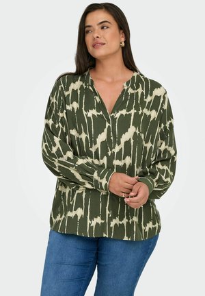 Blouse verte et crème à motifs avec un décolleté en V, manches longues et coupe décontractée, fabriquée en tissu léger. Associée à un jean en denim bleu.