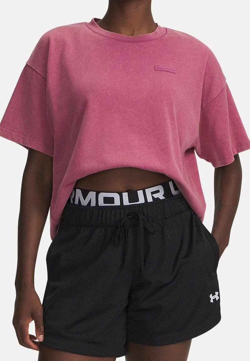 Rosa oversized t-shirt med en liten logotyp, kombinerad med svarta mesh-shorts som har en vit märkesmidja och dragsko.