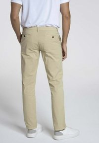 Chinos beige avec une coupe slim, dotés de poches arrière et d'une texture lisse, associés à des baskets blanches et un t-shirt blanc uni.