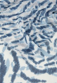 Écharpe légère présentant un motif abstrait bleu et blanc avec une texture visible. Les bords sont légèrement effilochés, ce qui rehausse l'apparence douce du tissu.