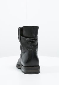 Bota de piel negra hasta el tobillo con un diseño arrugado, textura suave, punta redonda y un tacón bajo apilado. La vista trasera muestra detalles de costura.