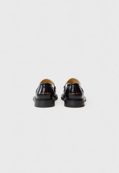 Svarta, polerade läderloafers med låg klack, sedda bakifrån, med "Filling Pieces" i guldtext på klacken.