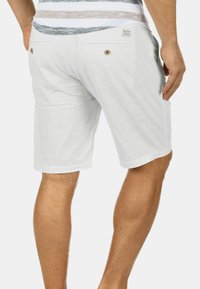 Shorts en lin blanc avec une coupe décontractée, dotés de deux poches arrière avec boutons et d'un tissu légèrement texturé.