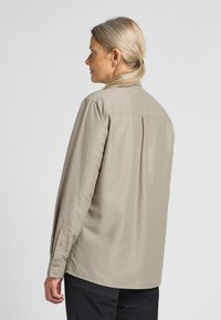 Helles beige Langarmhemd mit Kragen, einzelner Rückenfalte und Knopfmanschetten, aus glattem Stoff gefertigt.