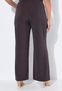 Donkerbruine, wijde broekspijpen van rekbare stof, met een gladde afwerking en een elastische tailleband. Gecombineerd met naakte hoge hakken.