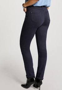 Donkerblauwe skinny jeans van rekbare stof, met achterzakken en opgerolde boorden, gecombineerd met zwarte enkellaarzen met hak.
