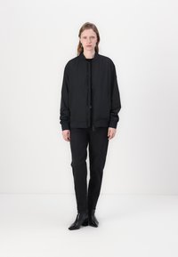 Black bomber jacket made of lightweight fabric, featuring a zip closure and elastic cuffs. Paired with black fitted pants and heeled boots.