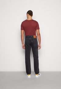 Jeans gris oscuro con un corte recto, que cuentan con una etiqueta de cuero en la parte posterior de la cintura y una camiseta ajustada de color burdeos suave. Zapatillas blancas incluidas.