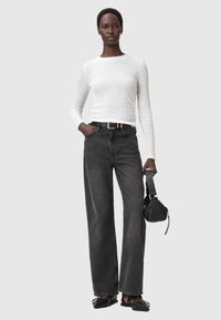 Witte, gestructureerde top met lange mouwen, gecombineerd met hoge taille, loszittende zwarte jeans. Accessoires omvatten een zwarte tas en glanzende zwarte schoenen.