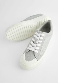 Grå sneakers med en texturerad ovandel, vit gummisula och vita snören. Har en låg design och förstärkt tåskydd.