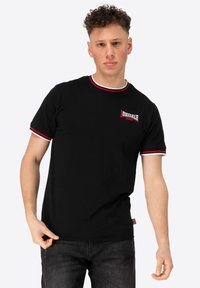 Musthave musta lühikeste varrukatega T-särk punase ja valge triibulise soonikkoes krae ning varruka servadega. Rinnal rikkalikult broderitud "Donsdale London" logo.