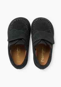 Scarpe per bambini in suede nero con una strap in velcro, punta rotonda e cuciture a contrasto. All'interno presentano una fodera in pelle marrone.