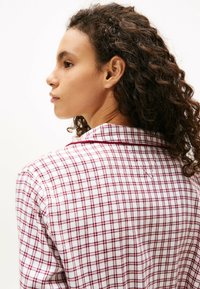 Biała koszula z kołnierzykiem w czerwono-granatową kratę, z krótkimi rękawami i teksturowaną tkaniną. Widok z tyłu pokazuje kołnierzyk koszuli.