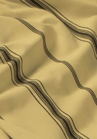 Gult tyg med vågiga svarta ränder; slät textur och draperat utseende. Subtila nyansvariationer förhöjer mönstrets visuella intresse.