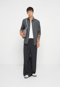Camisa gris de botones, camiseta blanca debajo, pantalones anchos oscuros y bolso gris. Zapatillas deportivas con detalles en blanco y gris. Diseño minimalista.